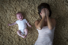 Femme qui se couvre le visage car elle supporte difficilement les pleurs du bébé à côté d’elle.